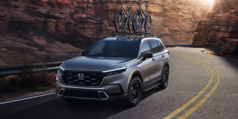 A grey 2025 Honda CR-V with a bike rack on top driving down a mountain road