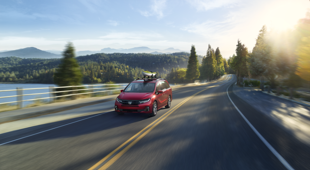 A red 2025 Honda Odyssey driving down a lakeside road
