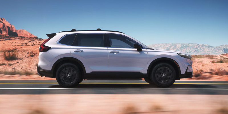 a white 2025 Honda CR-V Hybrid driving down a road in a desert